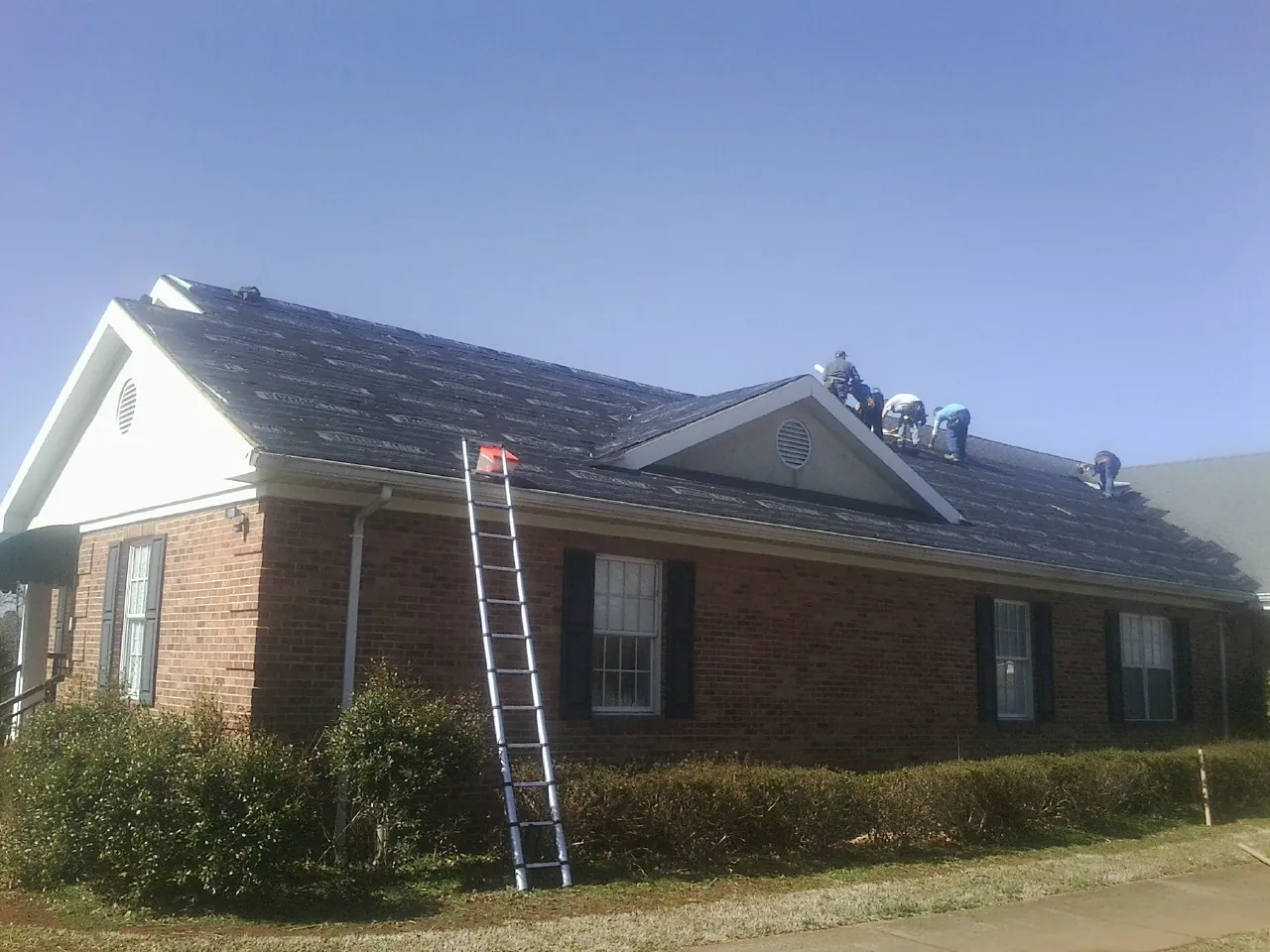 Crew tearing shingles off a brick ranch roof with a ladder set — Metal Roof Repair work by our crew in Castalia