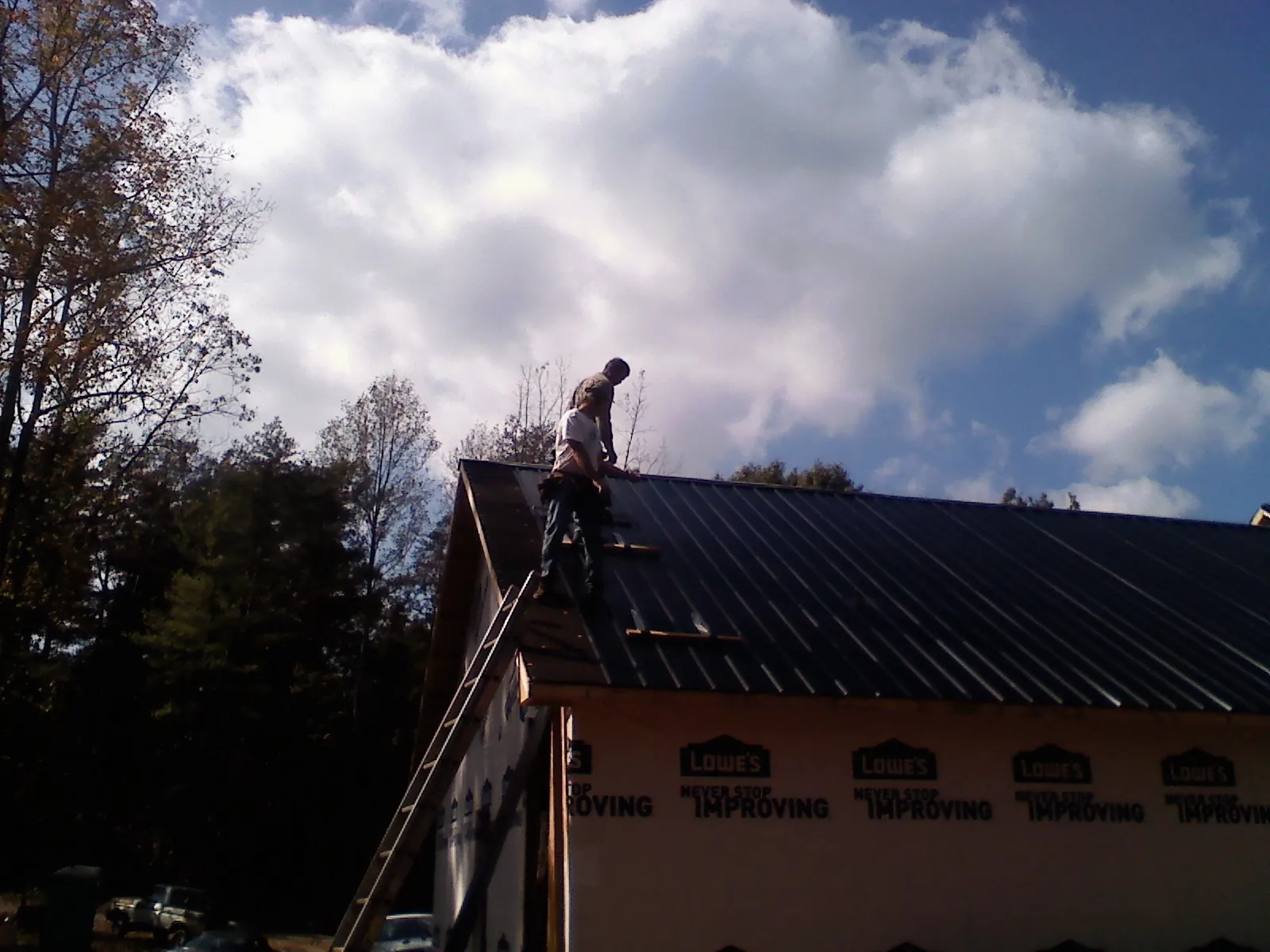 Roofer fastening dark metal panels high against a cloudy sky, from a Roof Inspection job in Castalia