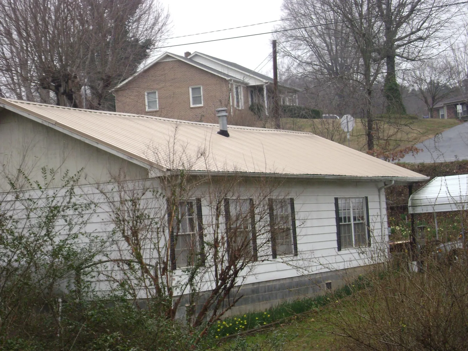 Tan metal roof on a white sided house set into a hillside — Commercial Roofing by Roofing Brothers in Castalia